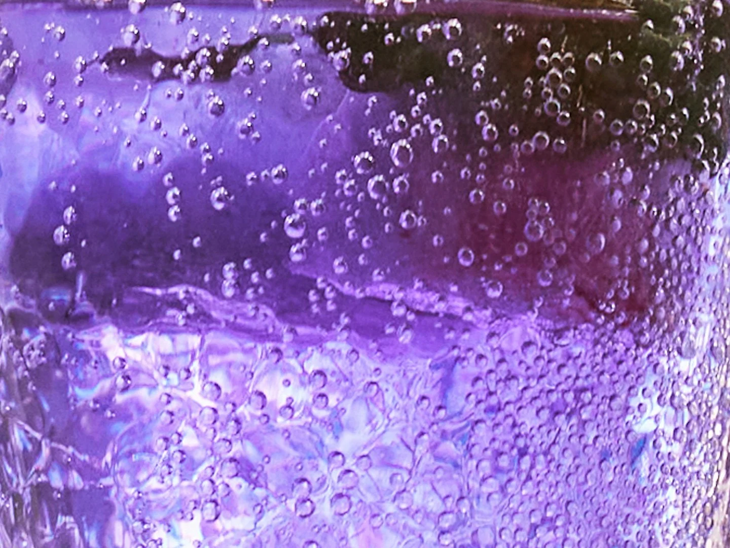 Close-up of a purple beverage with ice cubes and condensation on the glass, with many tiny bubbles.