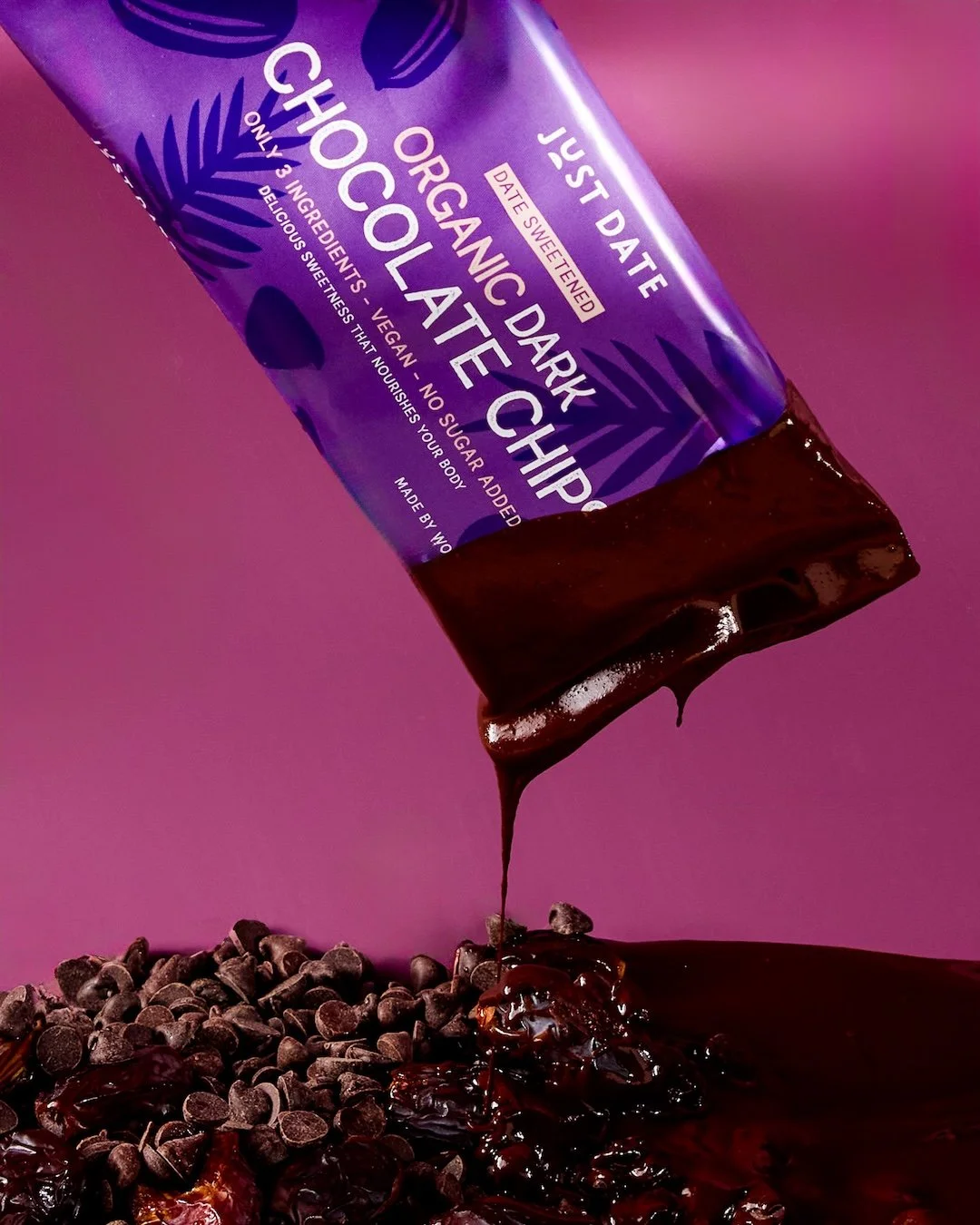A purple packaged dark organic chocolate chip bar pouring melted dark chocolate onto a pile of chocolate chips against a pink background.