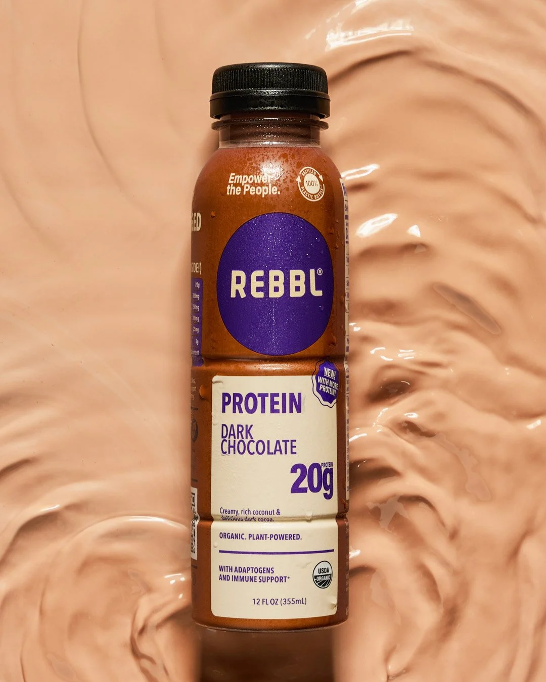 A bottle of REBBL protein dark chocolate drink on a swirled, light brown background.