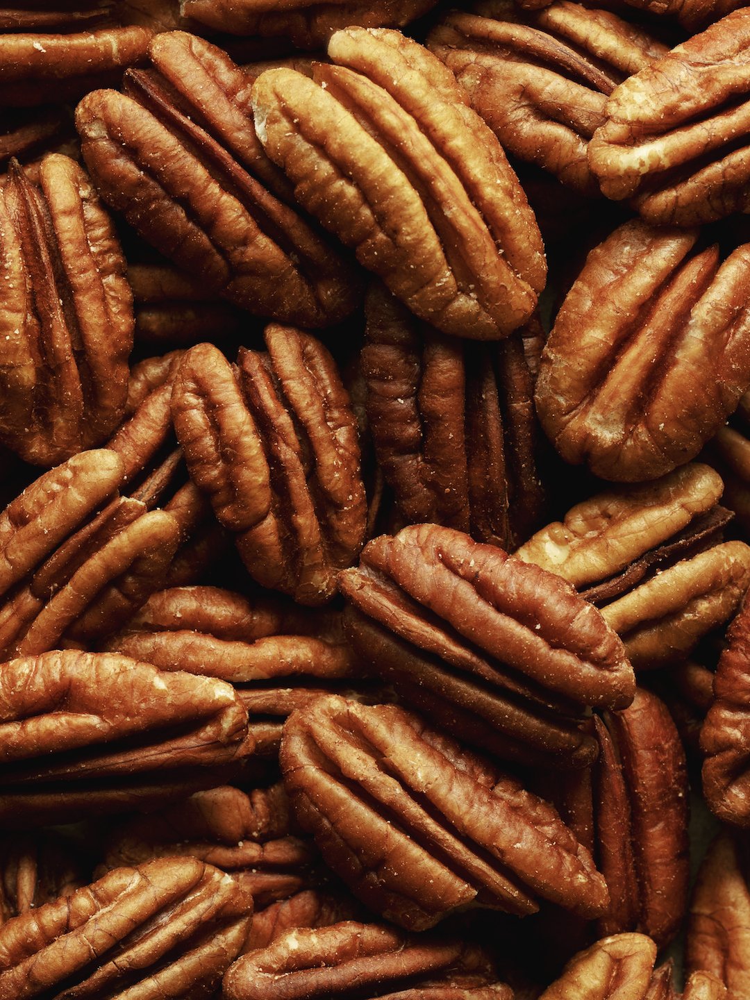 Close-up of roasted pecans showing their wrinkled, brown shells and nut inside.