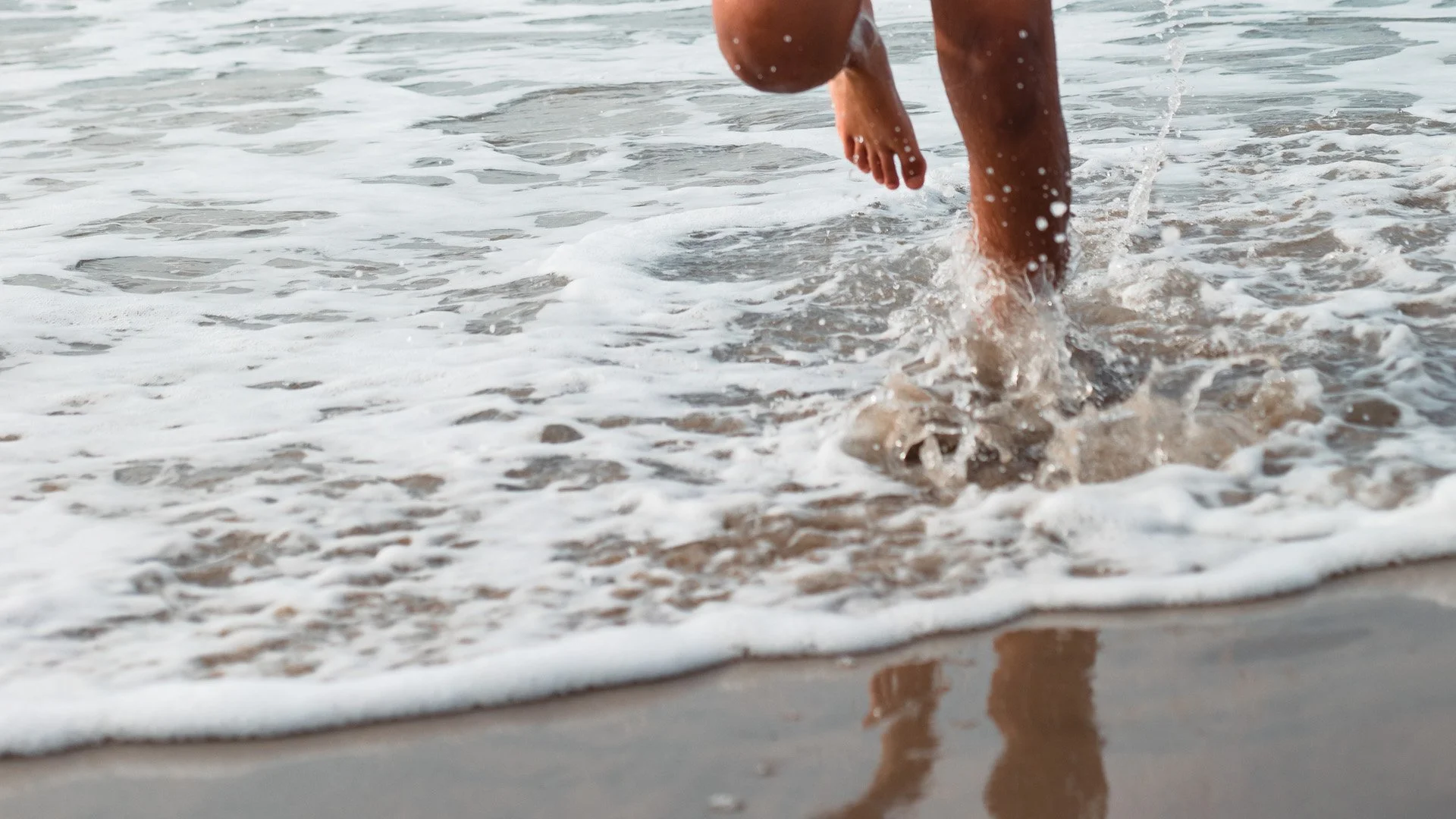 Person walking into ocean waves at the beach.