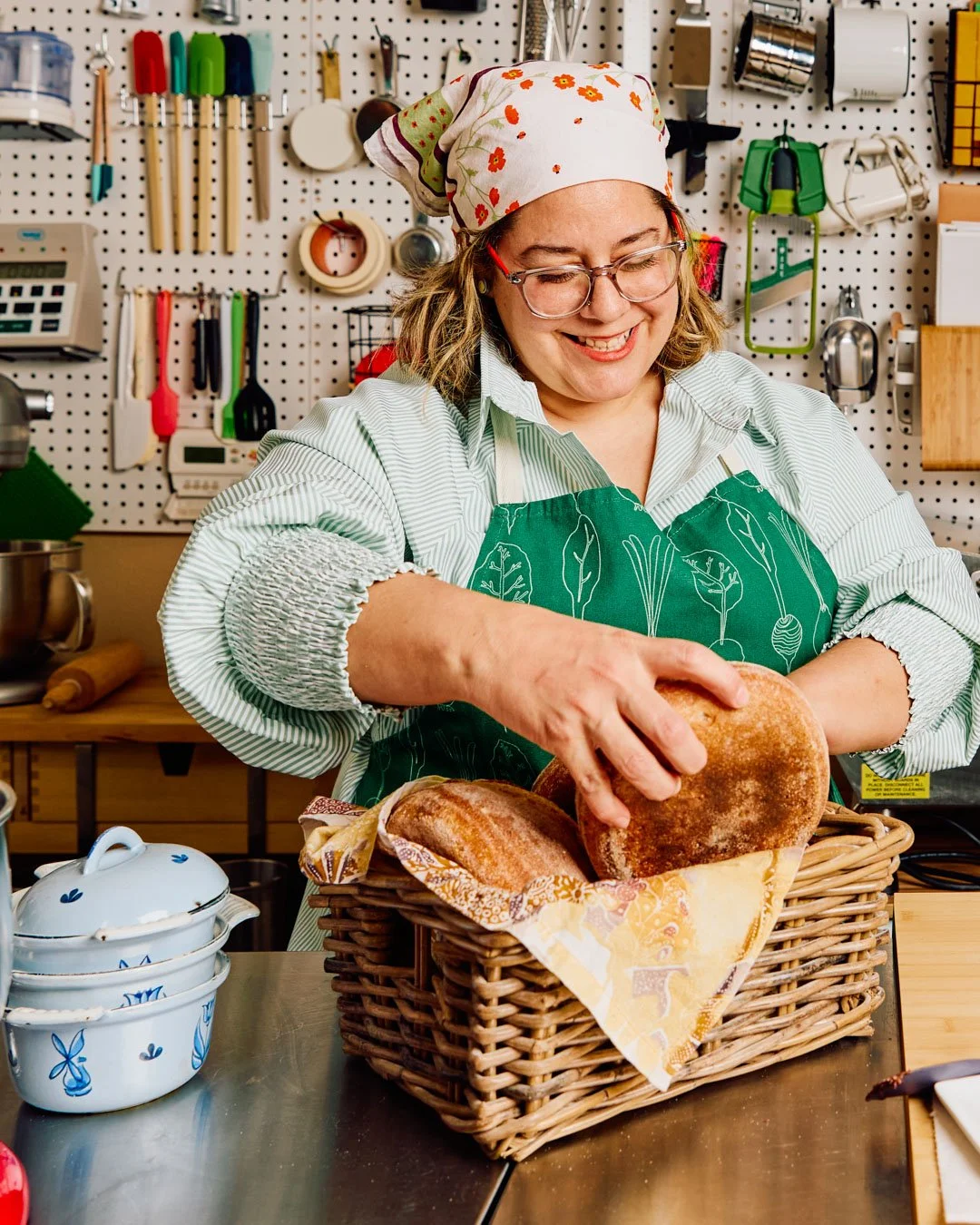 Woman smiling as she places freshly baked bread into a basket in a kitchen.