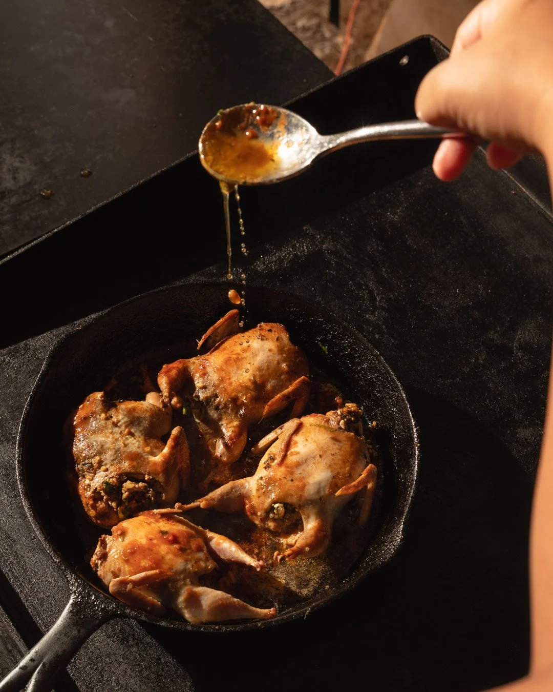 Chicken thighs cooking in a cast iron skillet with sauce being poured over them.
