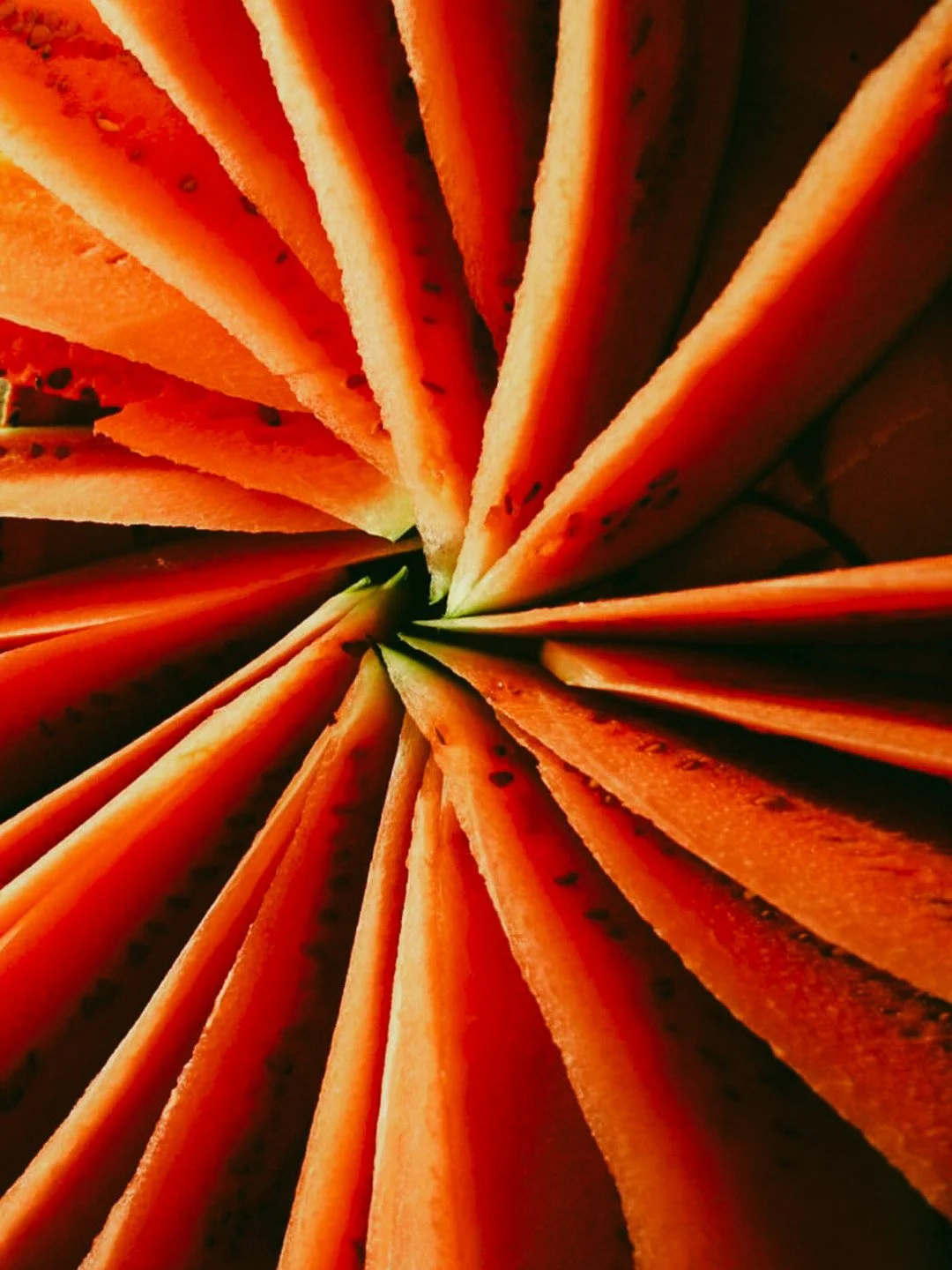 Close-up of a sliced papaya arranged in a circular pattern with orange flesh and black seeds.
