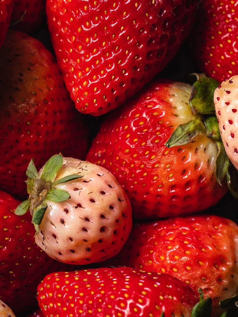 Close-up of ripe and unripe strawberries with green leaves.