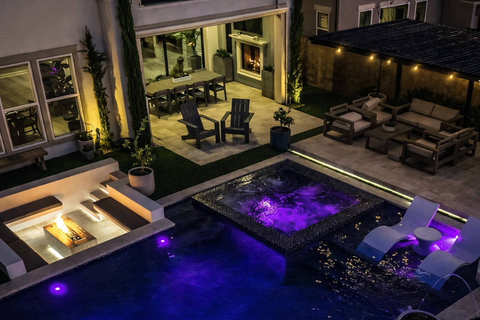 Night view of a backyard pool area illuminated by purple and yellow lights, with seating arrangements, a fire pit, and a dining area in the background.