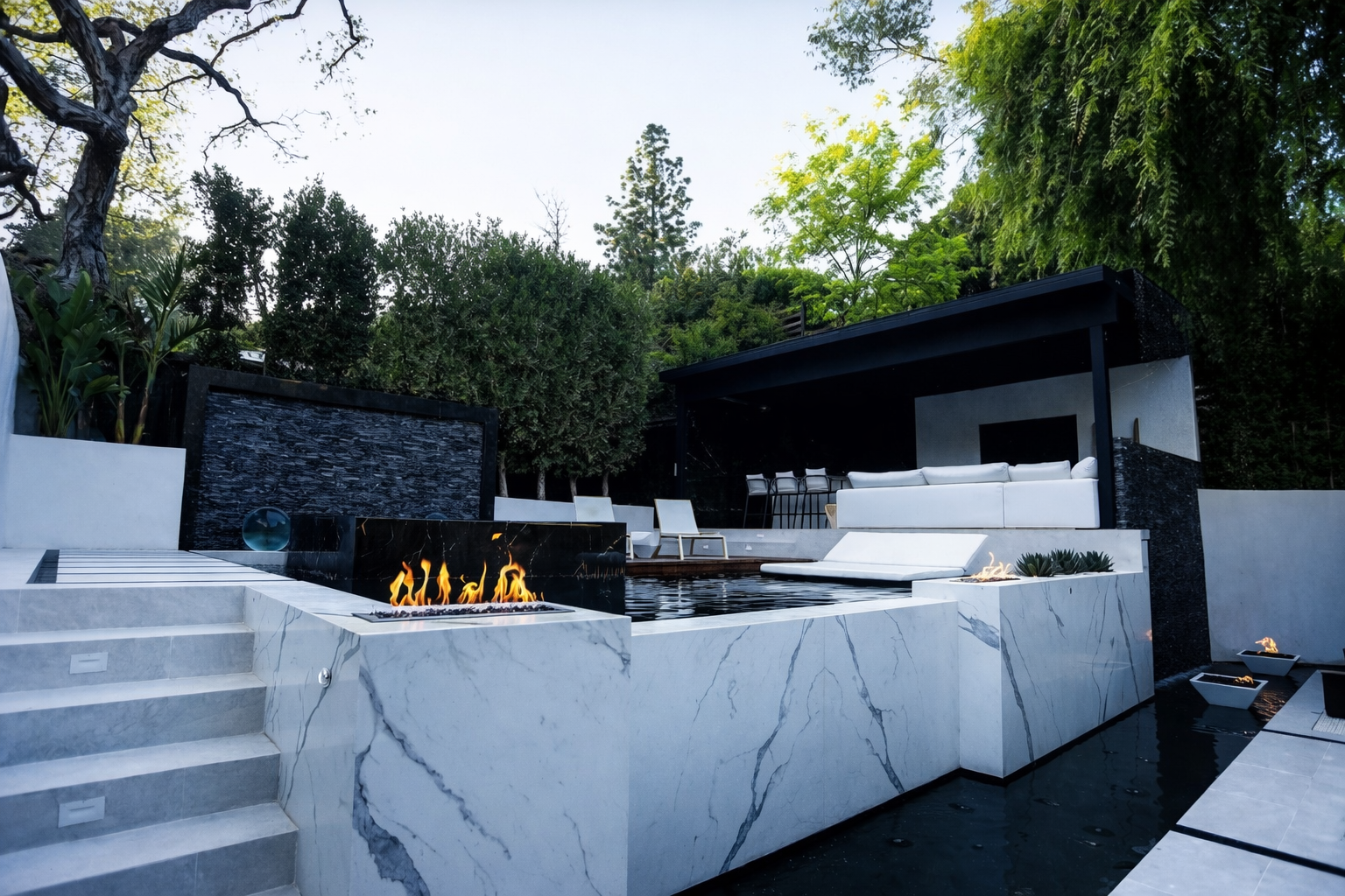 Modern backyard patio with pool, white seating, fire feature, and landscaped greenery