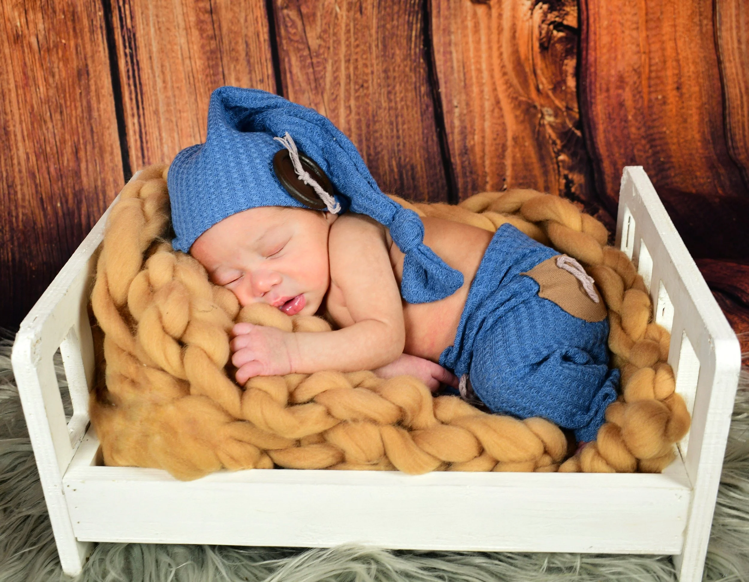 Newborn photography session featuring a sleeping baby styled in a soft blue outfit with brown patch details, photographed in a cozy in home setting. This timeless newborn portrait captures the beauty and peacefulness of a baby’s first days.