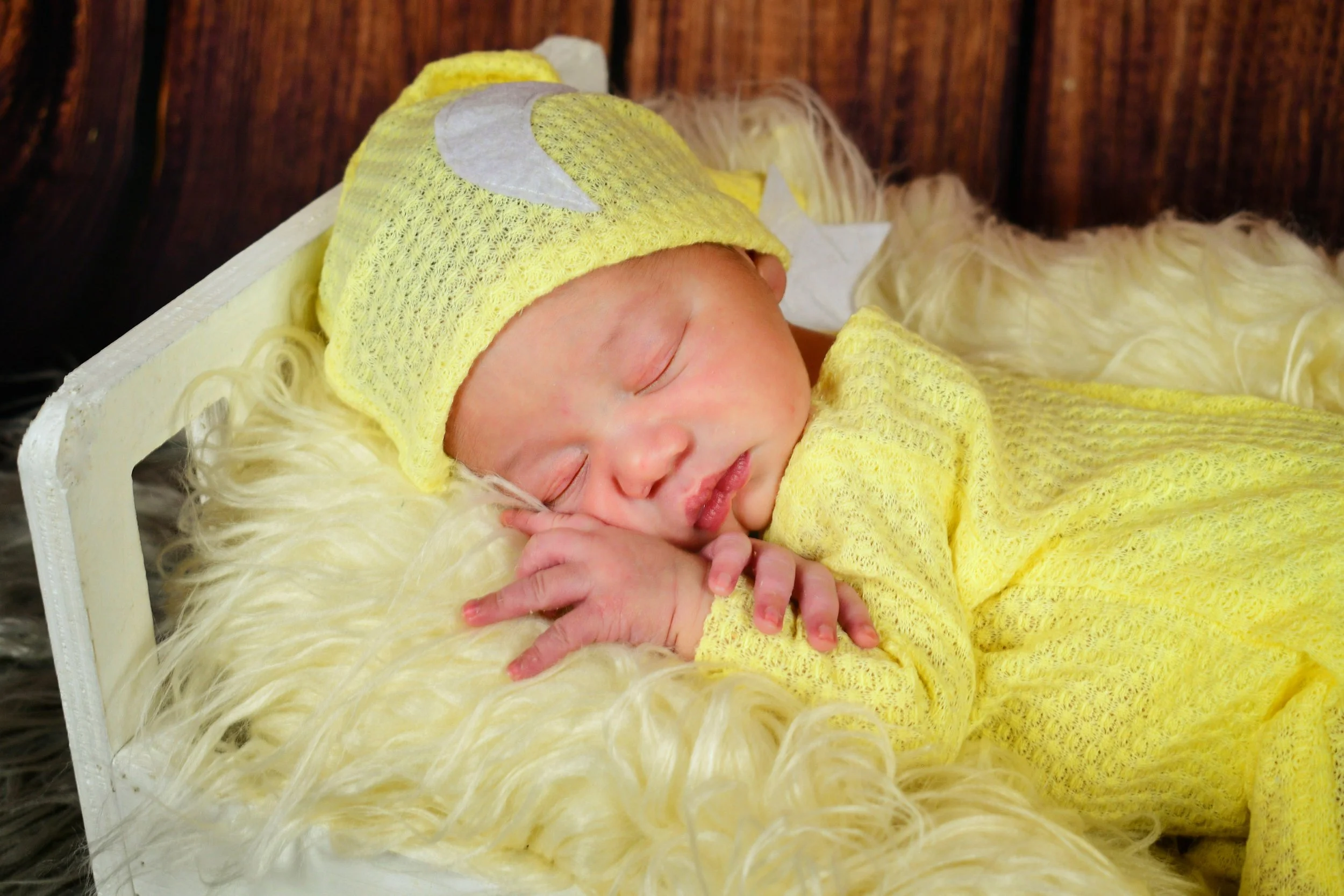 A peacefully sleeping newborn rests gently in a cozy bed, wrapped in a soft yellow outfit with delicate moon and star details. Surrounded by plush textures and warm tones, this portrait captures the innocence and serenity of baby’s earliest days.