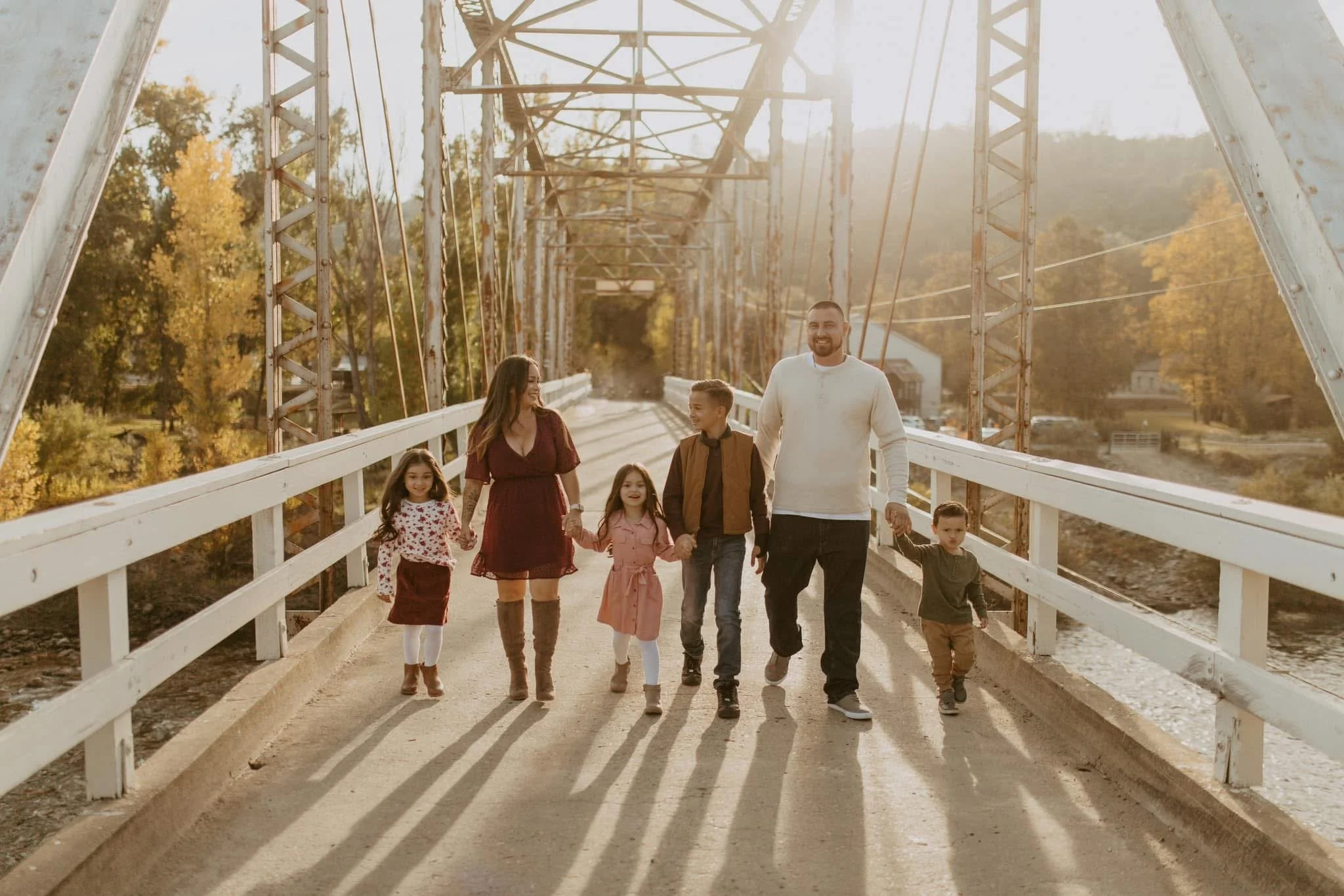 Family of six walking on a bridge during sunset, holding hands and smiling.
