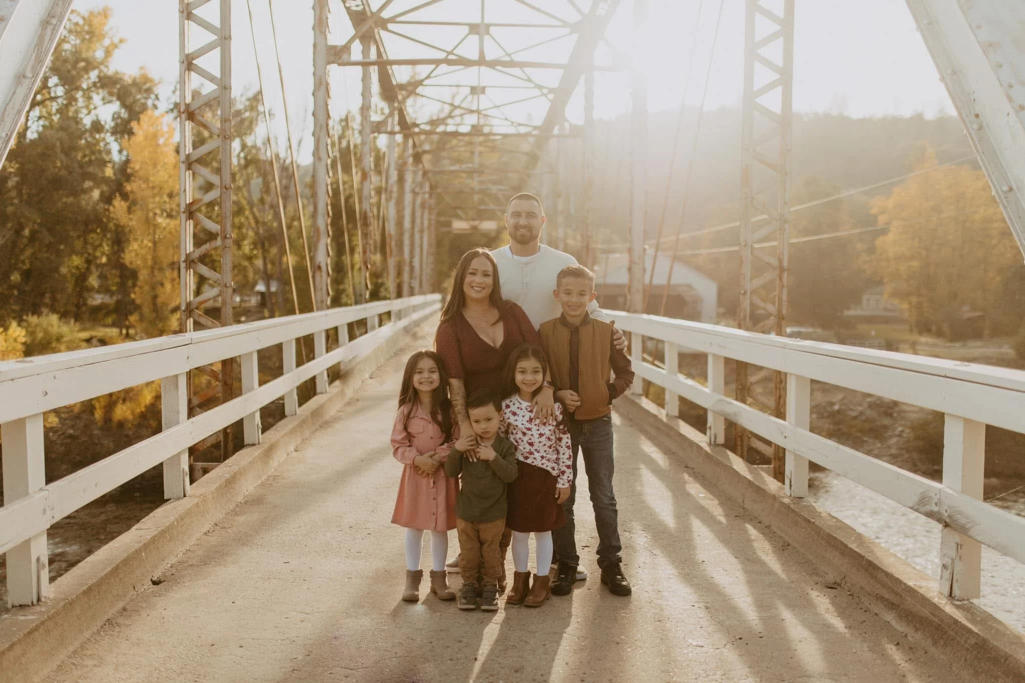 Family of six standing on a bridge during golden hour, smiling at the camera.