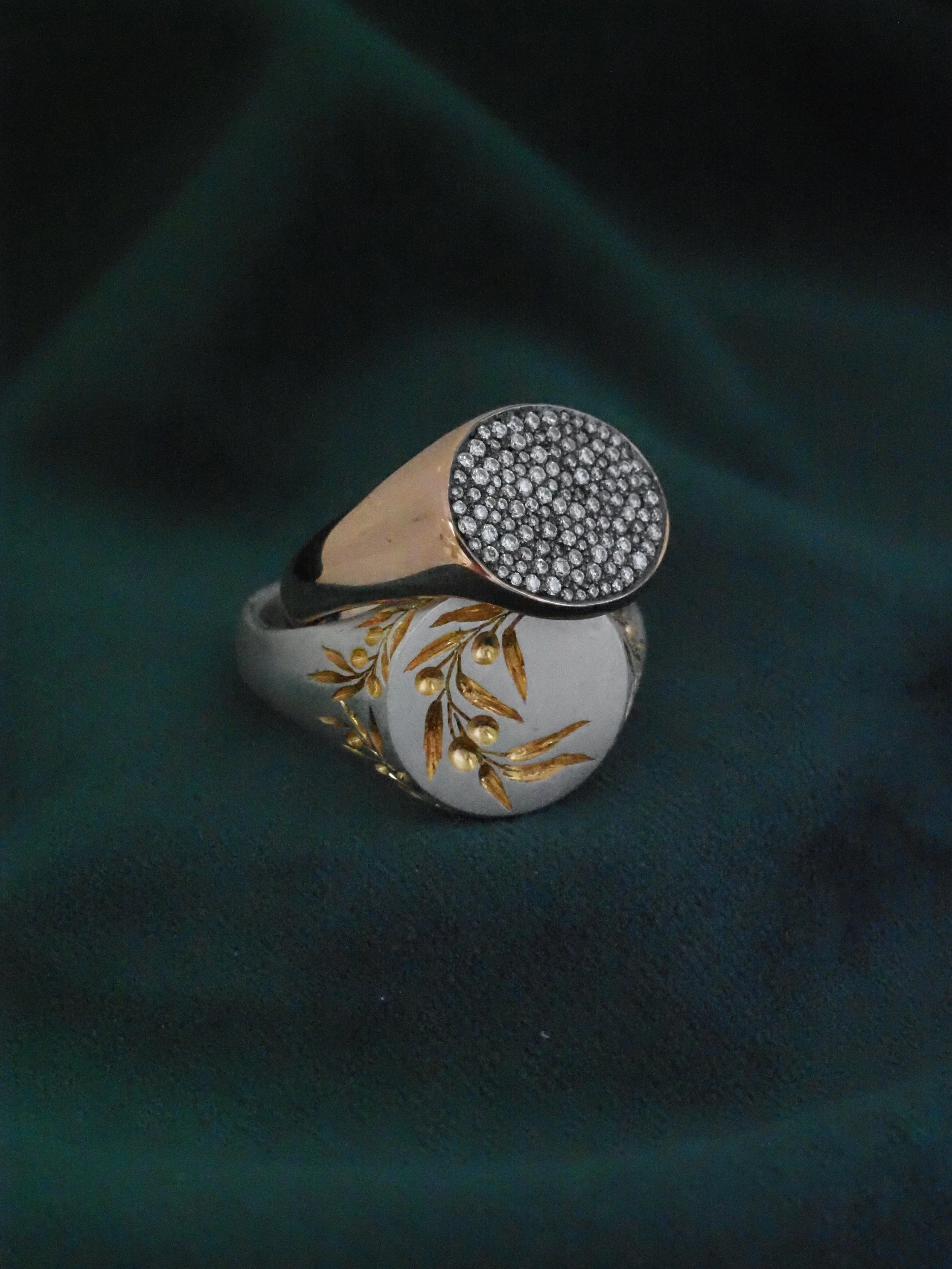 A ring with a black face encrusted with small diamonds, set on a piece of white jewelry with gold and floral decoration.