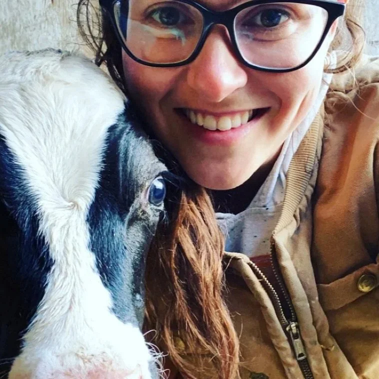 Woman with glasses smiling next to a calf