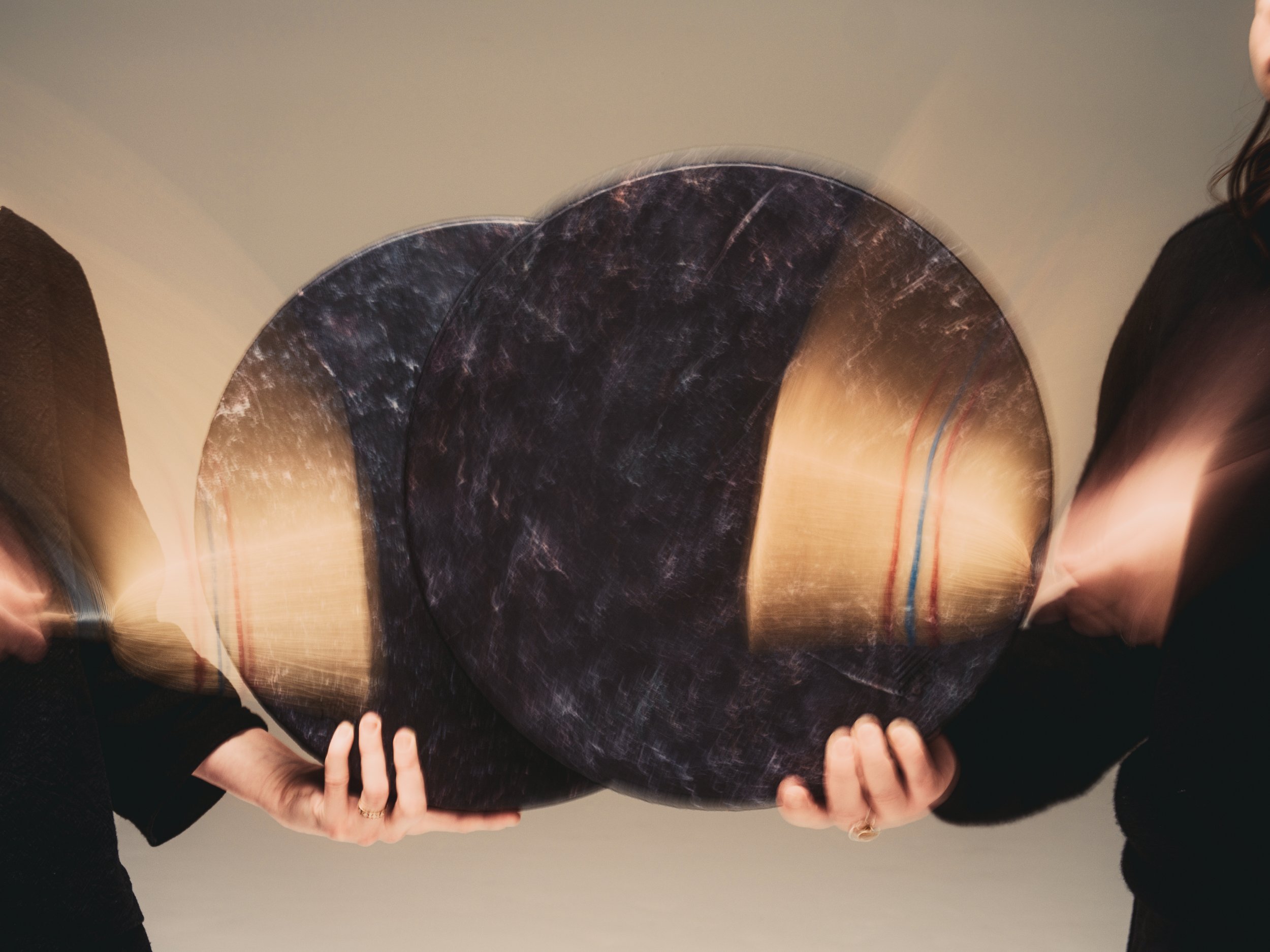 Two people holding circular ocean drums. The photo shows the movement of striking the drums with brushes.