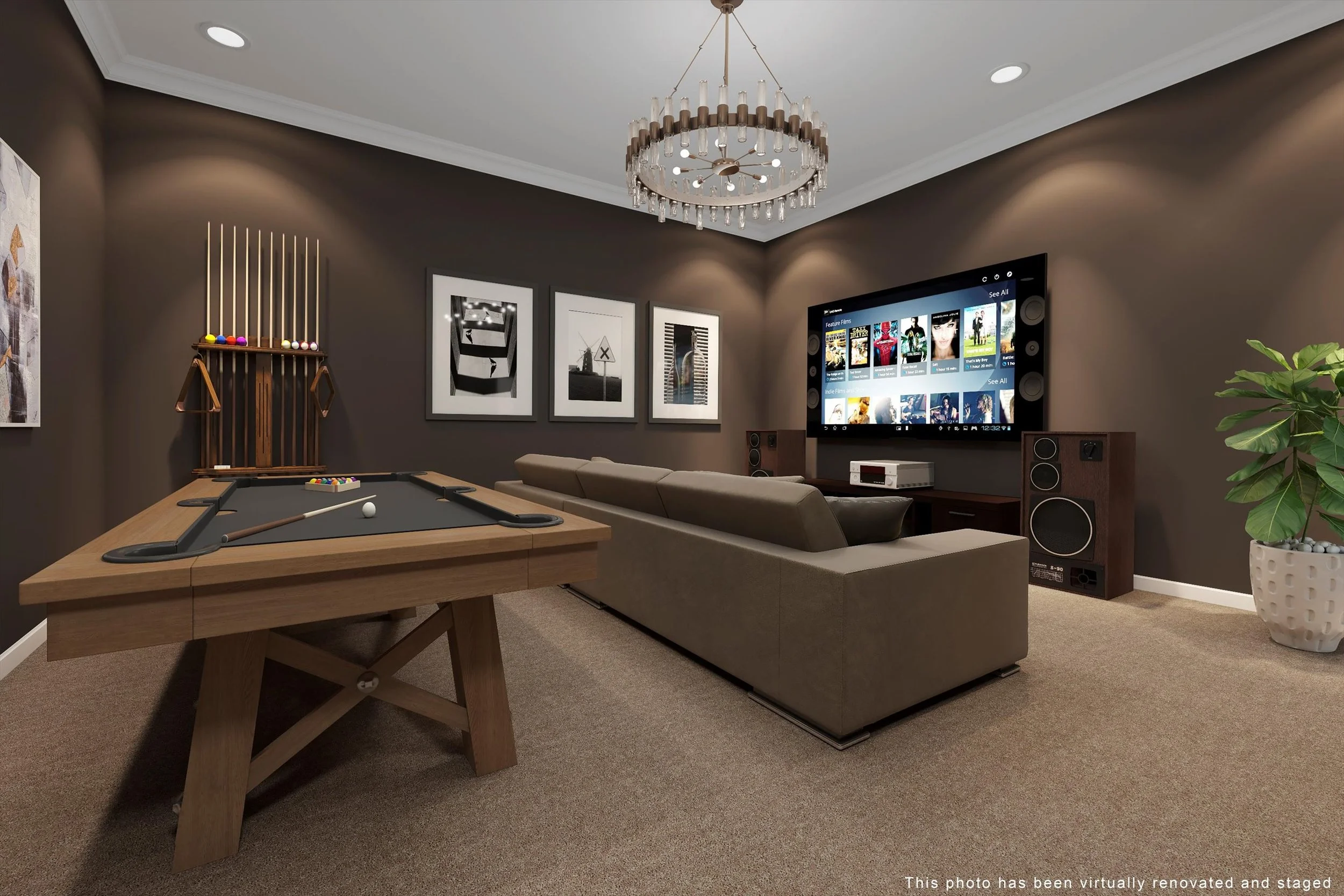 Living room with brown walls, a chandelier, a large television, a beige sectional sofa, a pool table, framed black and white artwork, a potted plant, and audio speakers.