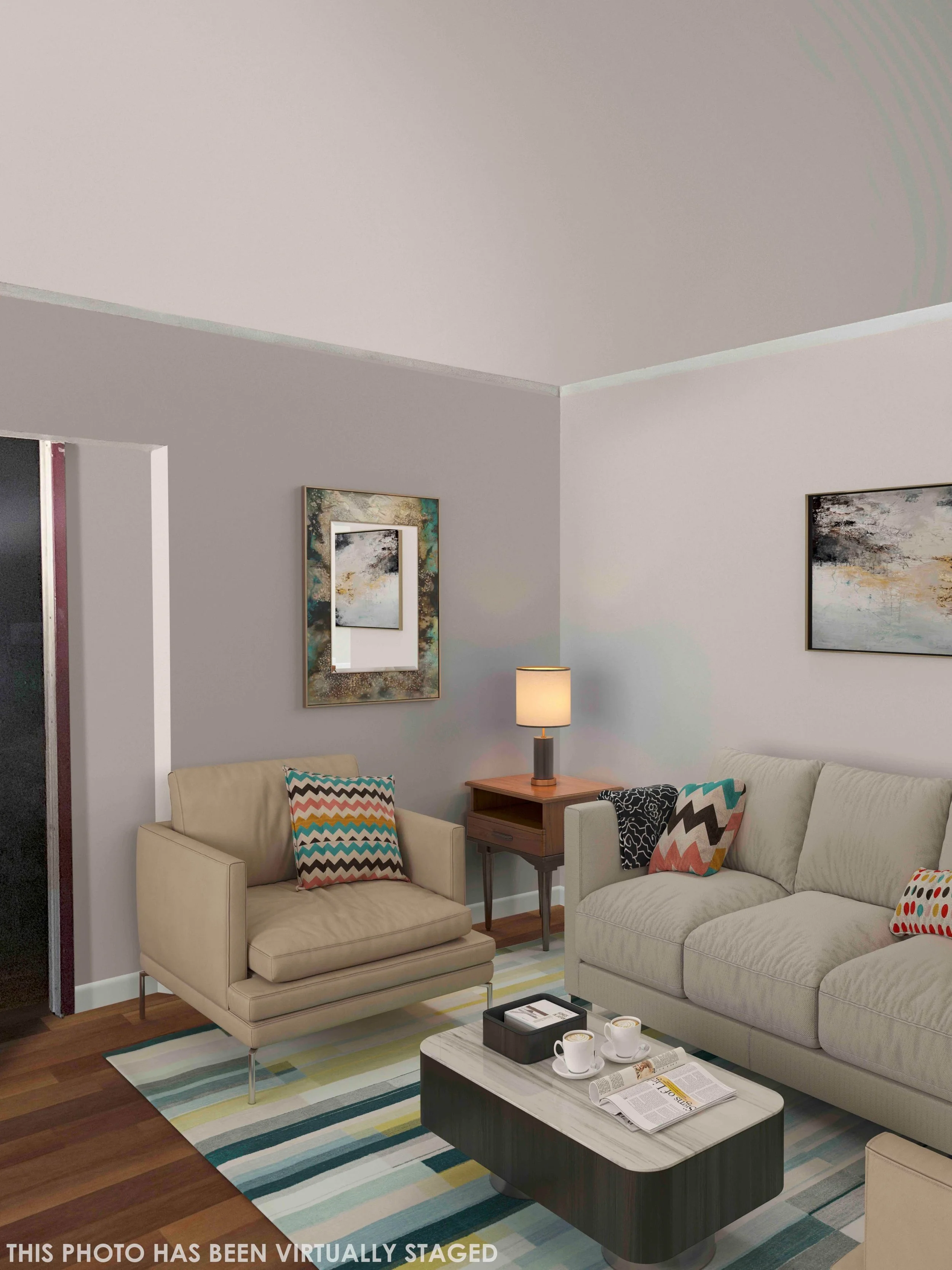 Living room with a beige armchair, a cream sofa, a wooden side table with a lamp, a coffee table with cups and magazines, colorful cushions, artwork on the walls, wooden flooring, and a striped rug.