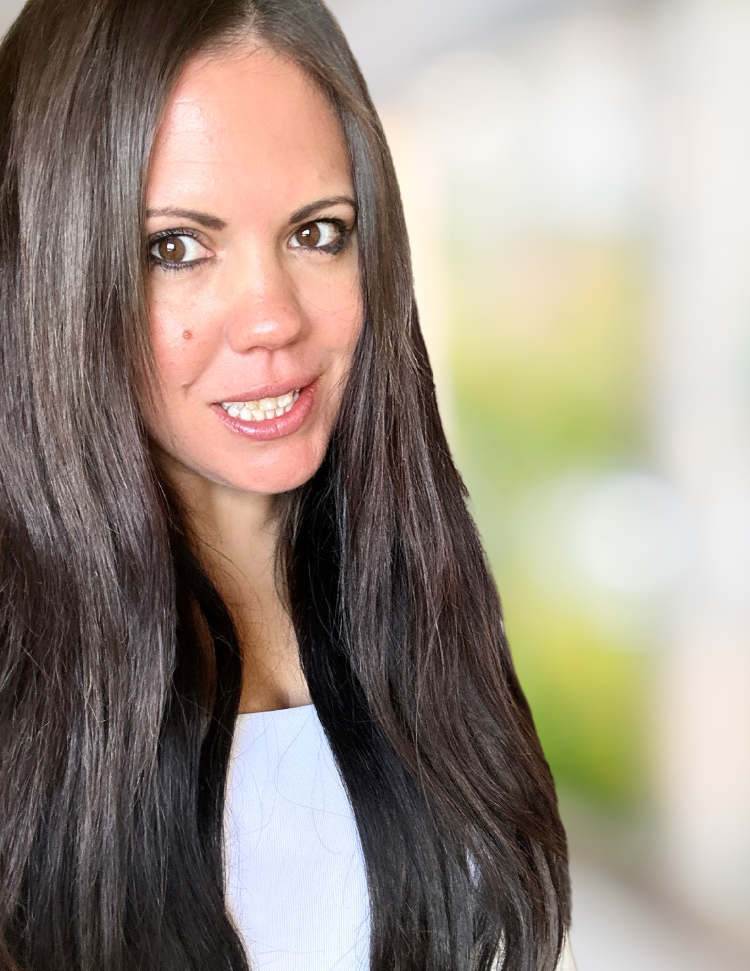 A woman with long, dark brown hair, light skin, and brown eyes looking at the camera, wearing a white top, with a blurred neutral background Andrea Hall Stachniewicz