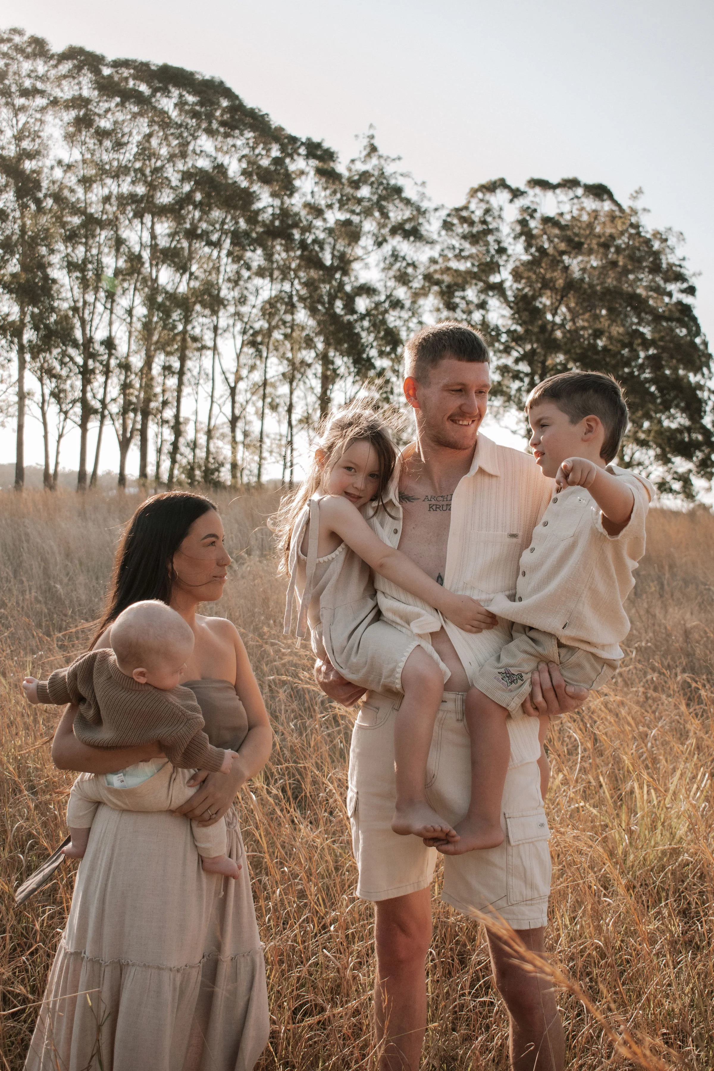 A family of five outdoors in a field of tall golden grass, with trees in the background, enjoying a sunny day.