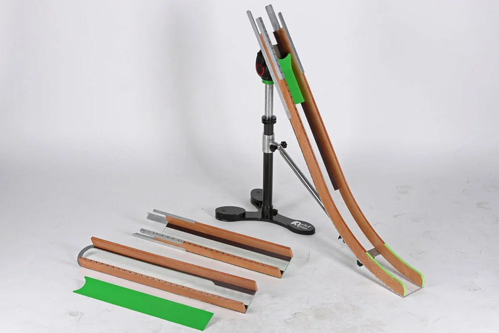 A toning table with accessories, including a stand, a green plastic tool, and several elongated flexible track sections with wooden inside and orange and green edges, used for physical therapy or muscle training.