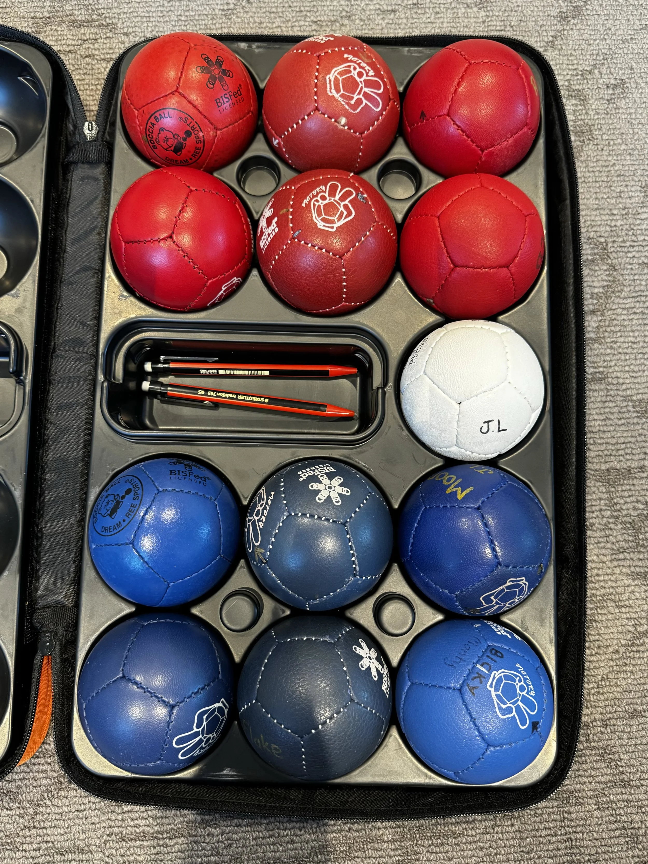 A set of sixteen red, white, and blue Boccia balls in a carrying case, along with two red and two black pins.