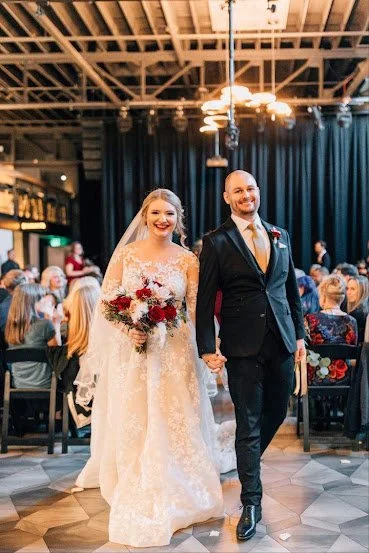 Bride and groom walking down the aisle during their wedding ceremony, holding hands and smiling, with guests seated in the background.
