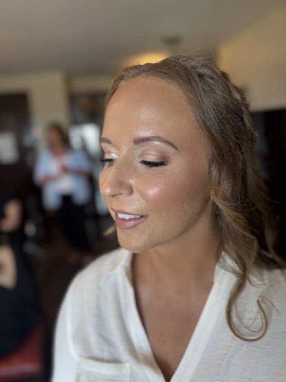 Close-up of a woman with makeup and wavy hair, smiling softly, in an indoor setting with blurred background.