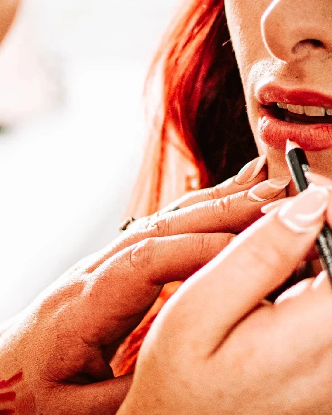 A woman with red hair applying lipstick with a mirror close-up of her face.