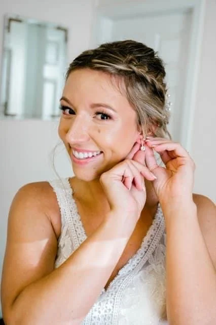 Woman smiling and putting on earrings, wearing a white lace top.