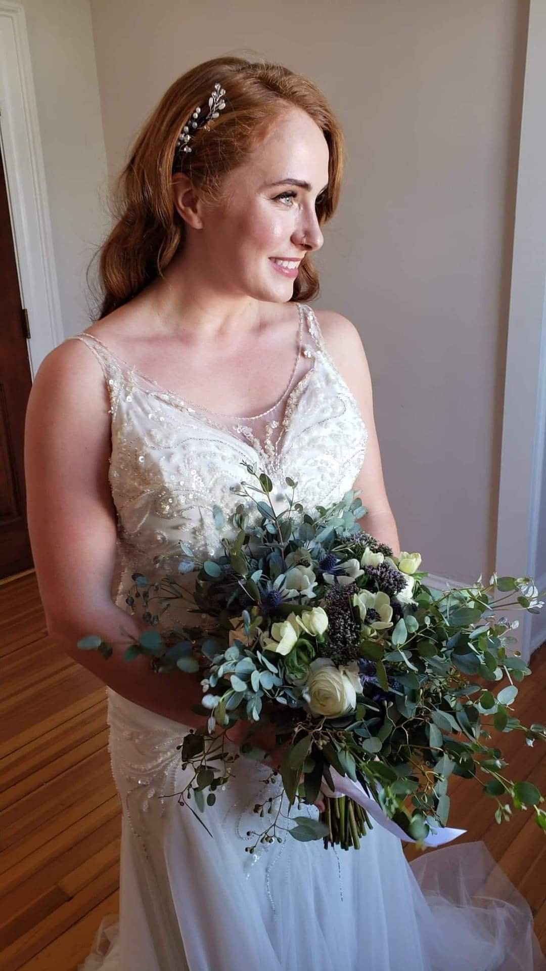 A bride in a wedding dress holding a bouquet of flowers, smiling and looking to her left.