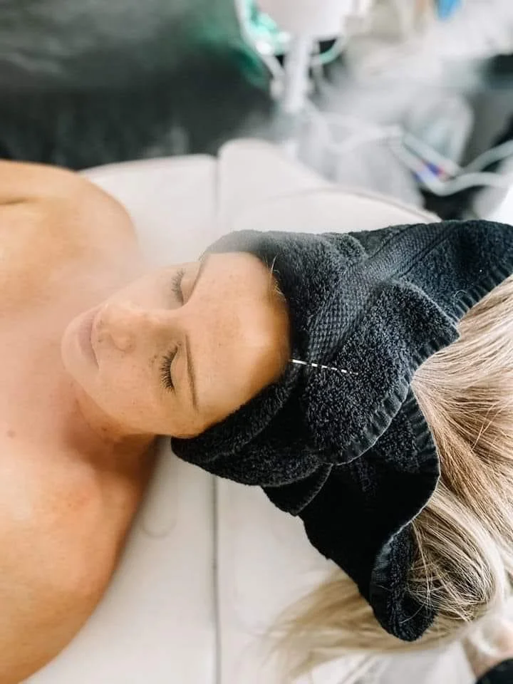 A person lying down with a black headwrap, eyes closed, and a visible ear and cheek, in a medical or clinical setting.