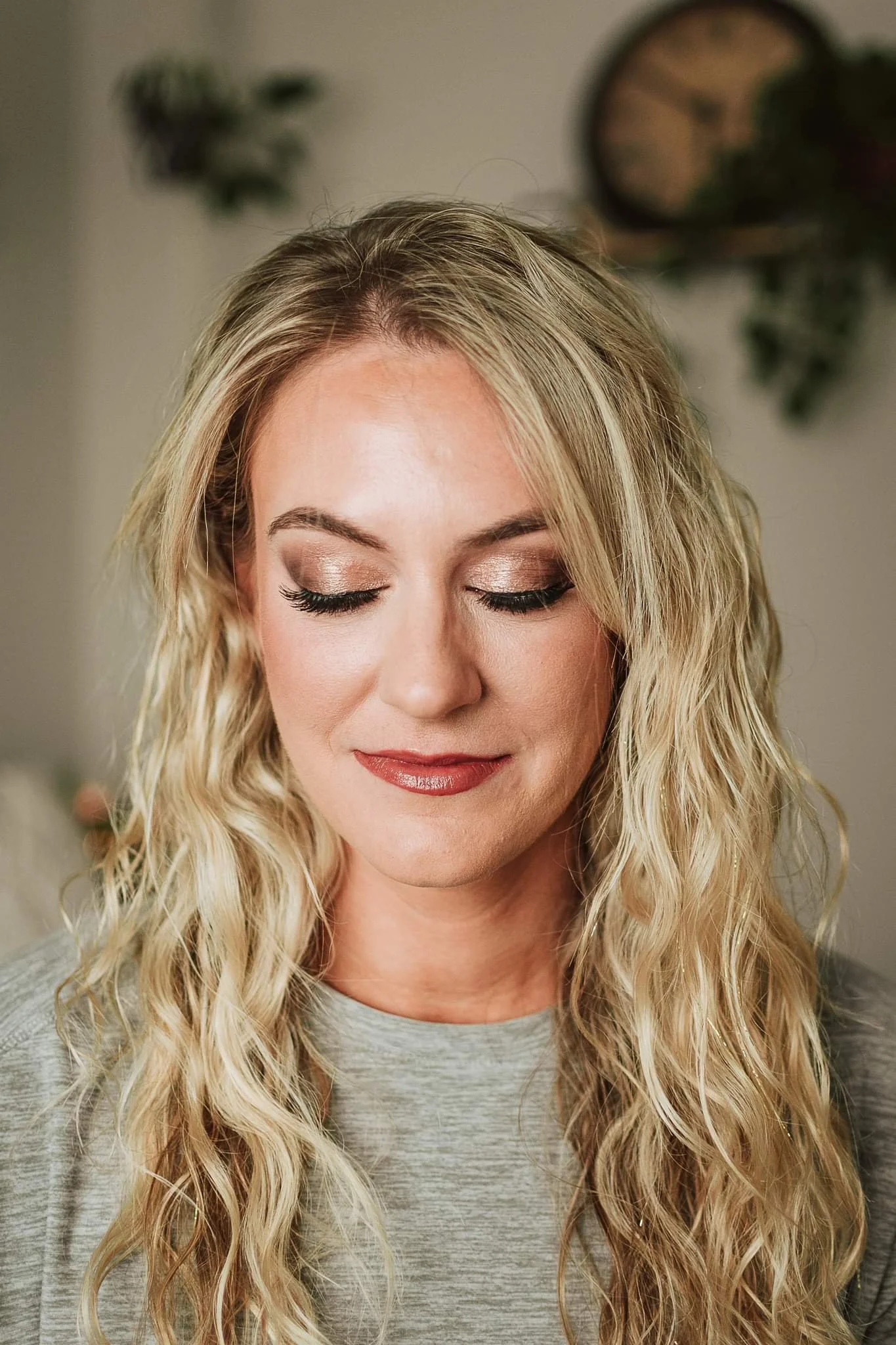 A woman with long, blonde, curly hair and makeup with closed eyes, smiling softly.