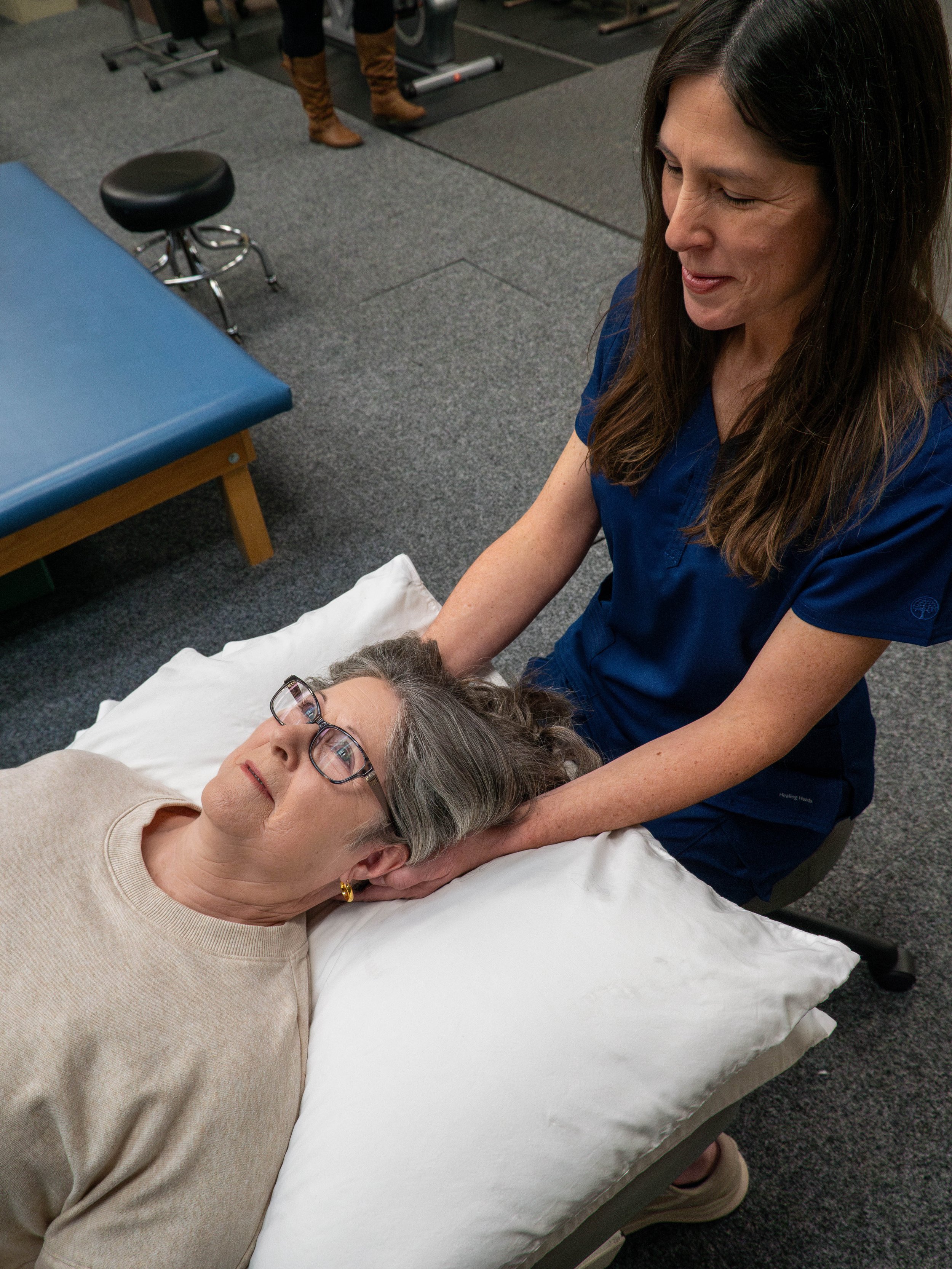A woman receiving a chiropractic neck adjustment from a healthcare professional in a medical office or therapy center.