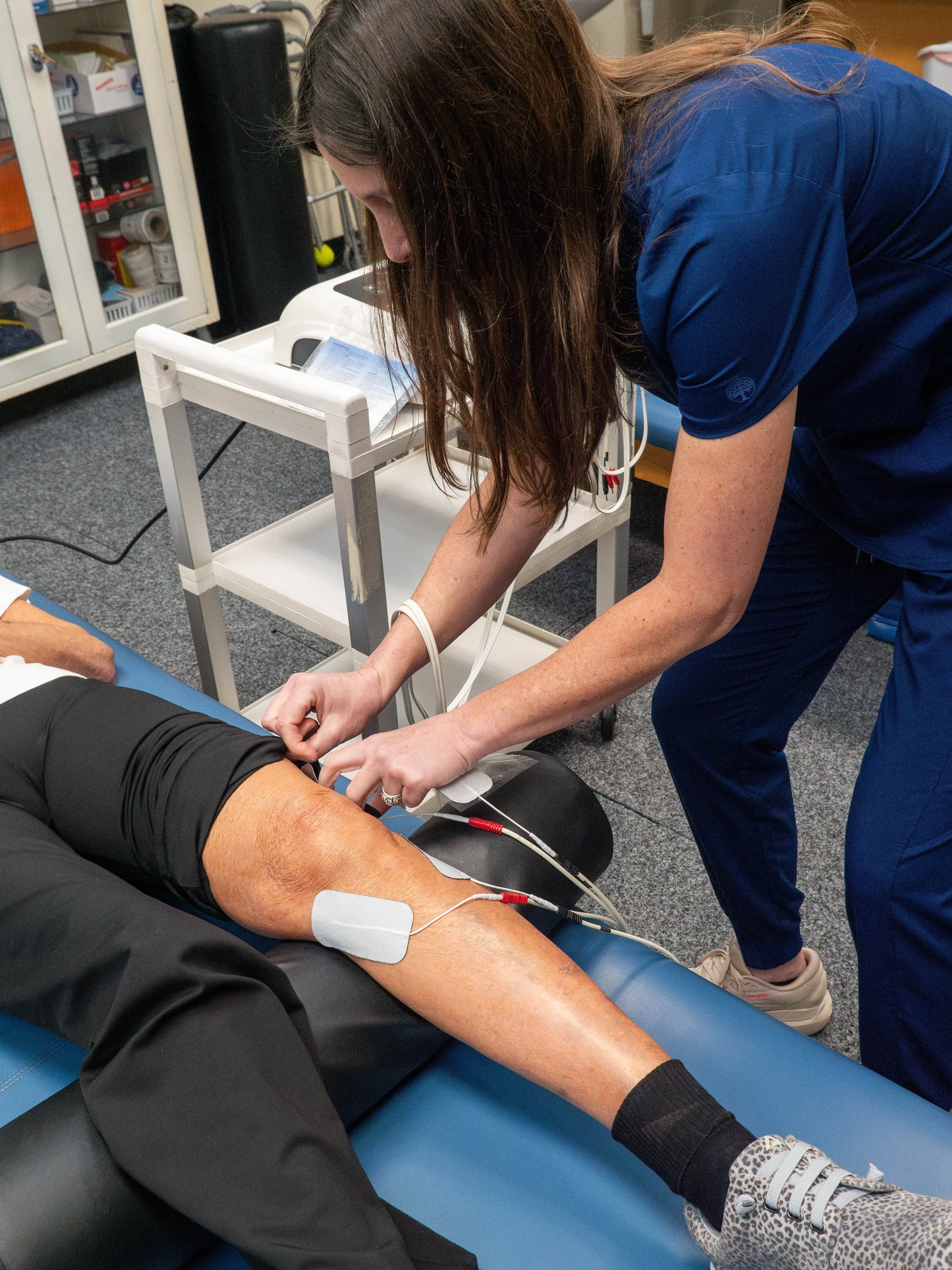 Medical professional checking a patient's leg with electrocardiogram leads attached in a clinical setting.