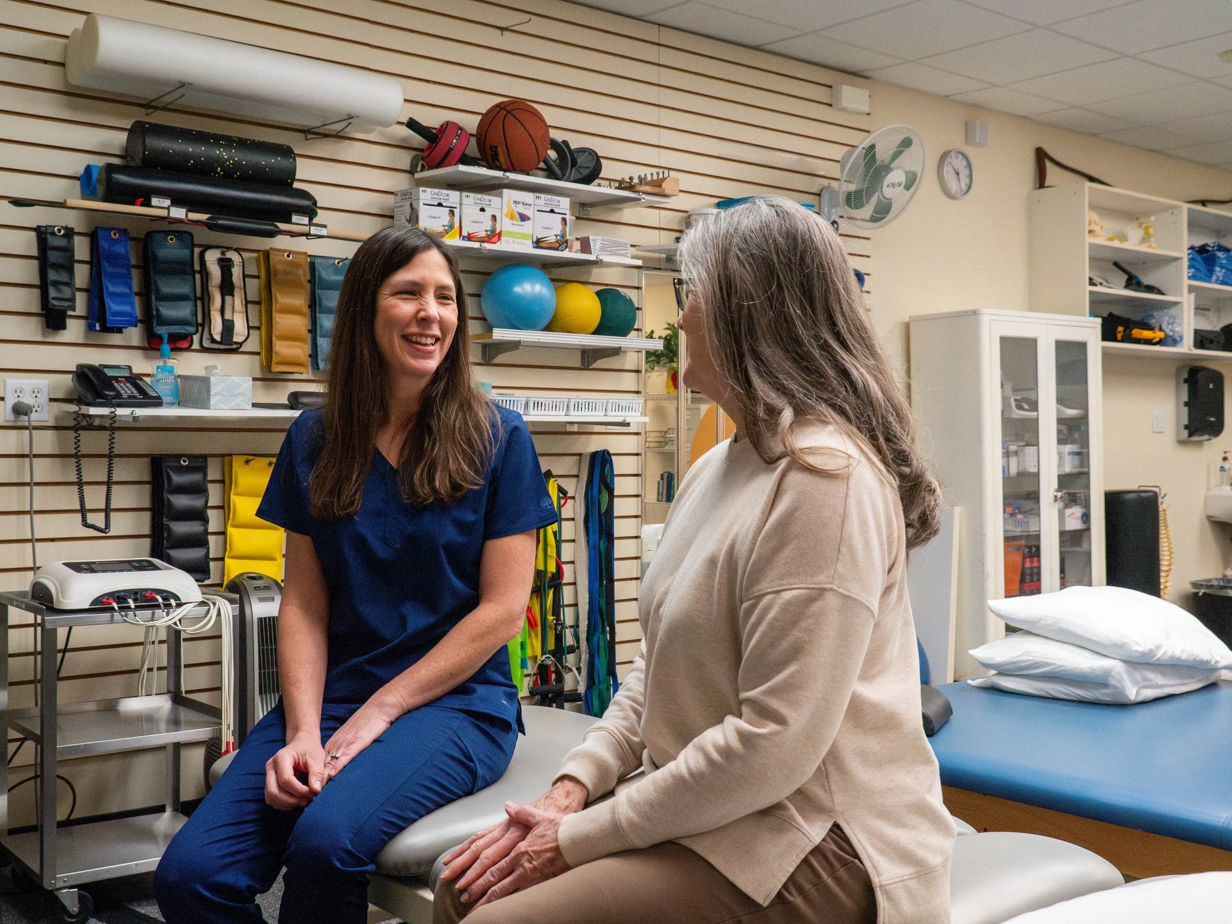 A healthcare professional and a patient sitting and talking in a medical examination room.