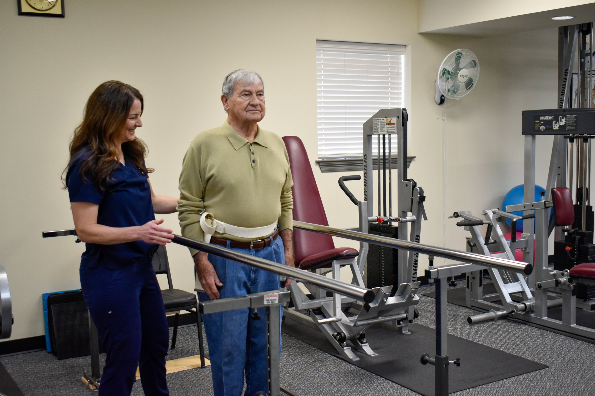 Physical therapy session with a woman assisting an elderly man using a cane in a rehab gym.