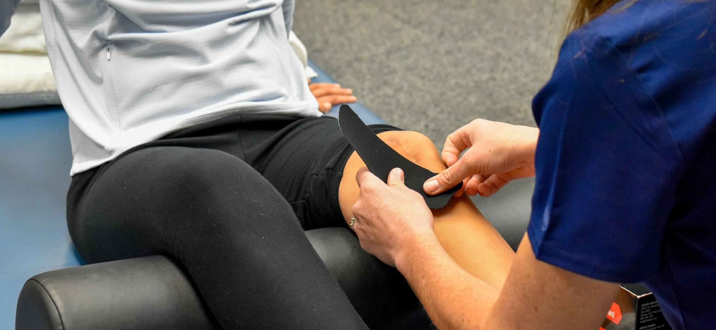 A healthcare professional is applying a black knee brace to a patient sitting on an examination table.