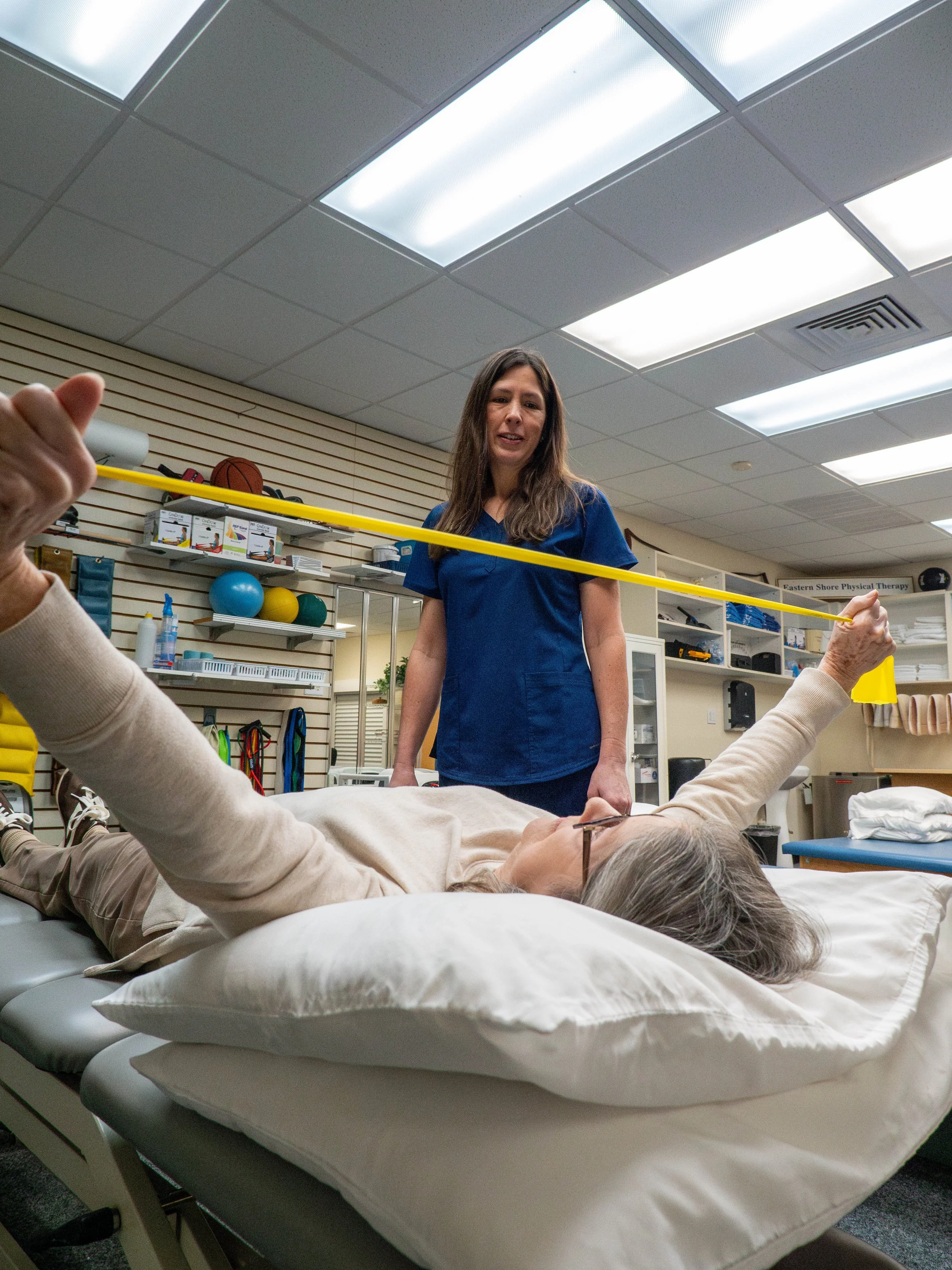 Physical therapist measures a patient's arm length with a yellow measuring tape in a healthcare setting.
