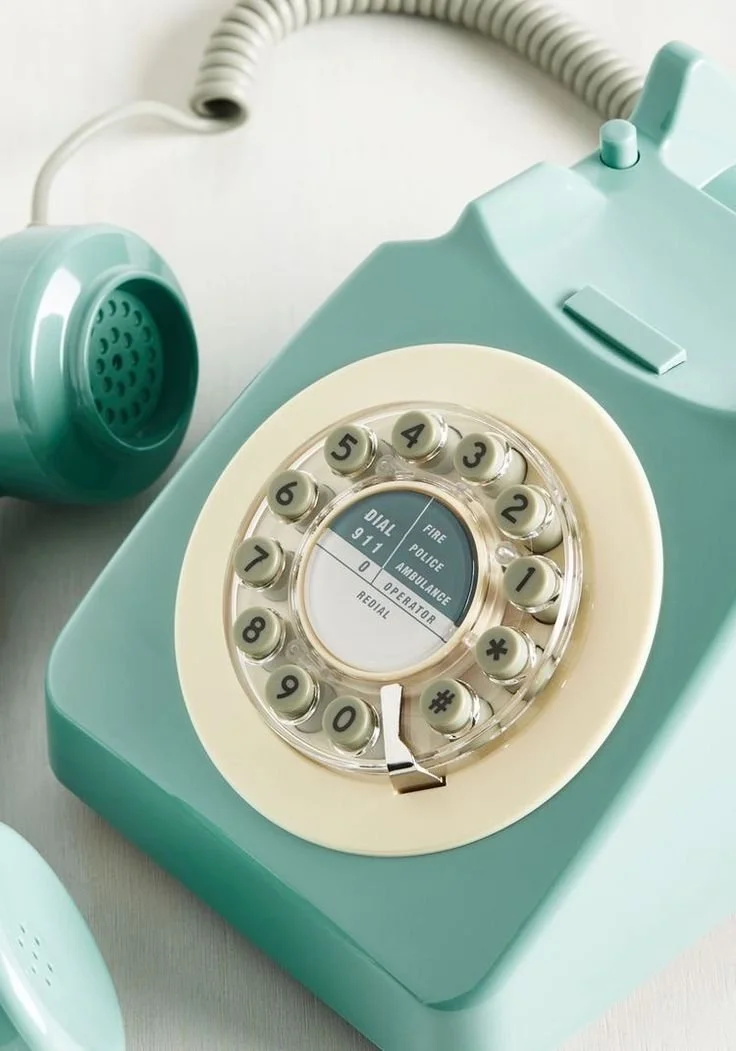 A vintage turquoise rotary phone with a circular dial that has a central screen showing emergency contacts.