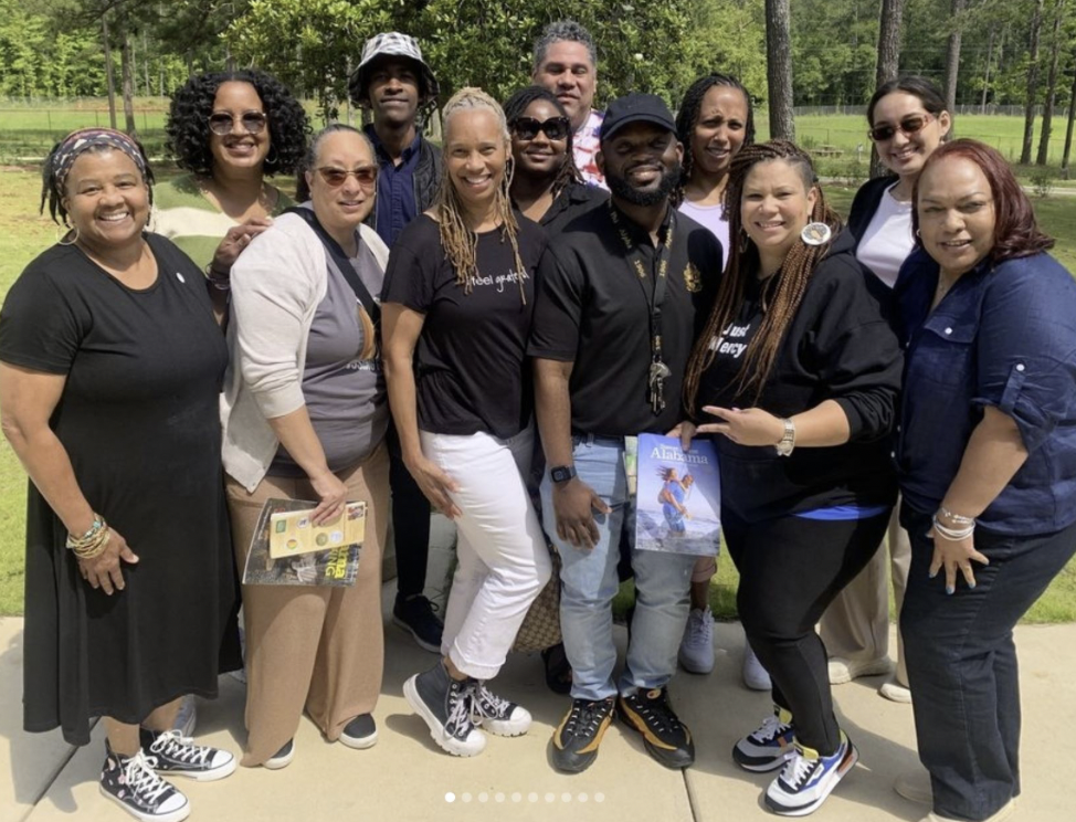 Group of people smiling outdoors in a park with green trees and grass in the background.