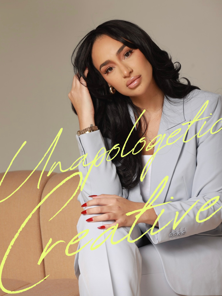 A woman with long black hair, wearing a light gray blazer and white shirt, sitting on a beige sofa. She has red nails, hoop earrings, and a gold bracelet, with her hand resting near her face. The text 'Unapologetic & Treat' is written in yellow cursive across the image.