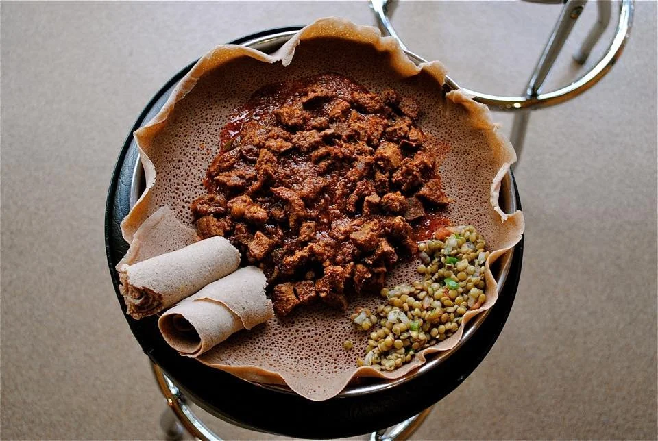 A cup of Ethiopian coffee with a traditional coffee filter filled with ground coffee, and kola bottles or roasted barley, on a table.