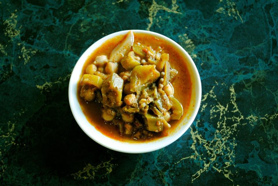 A small white bowl filled with a vegetable curry on a dark green, marbled surface.