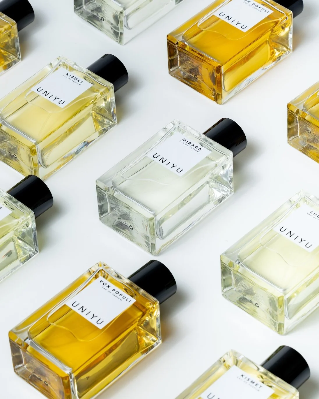 Multiple bottles of UNIYU perfume with white, yellow, and transparent liquid, arranged diagonally on a white background. Photography by Lila Marvell www.lilamarvell.com.au