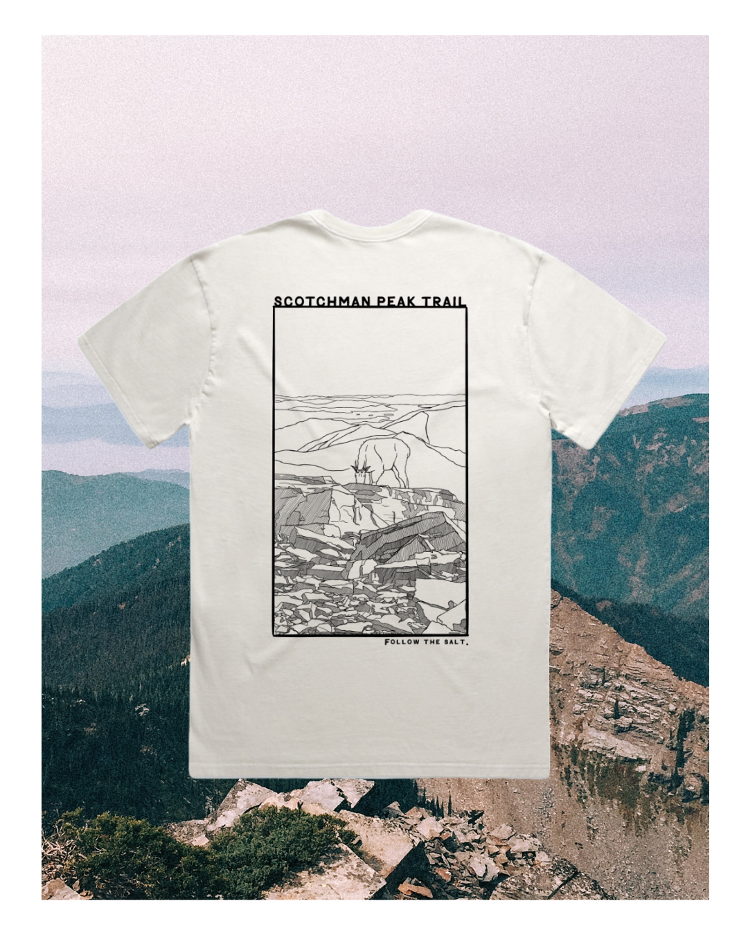 White T-shirt with line art of mountain landscape and a mountain goat, labeled 'Scotchman Peak Trail' at the top and 'Follow the Salt' at the bottom, set against a mountain backdrop.