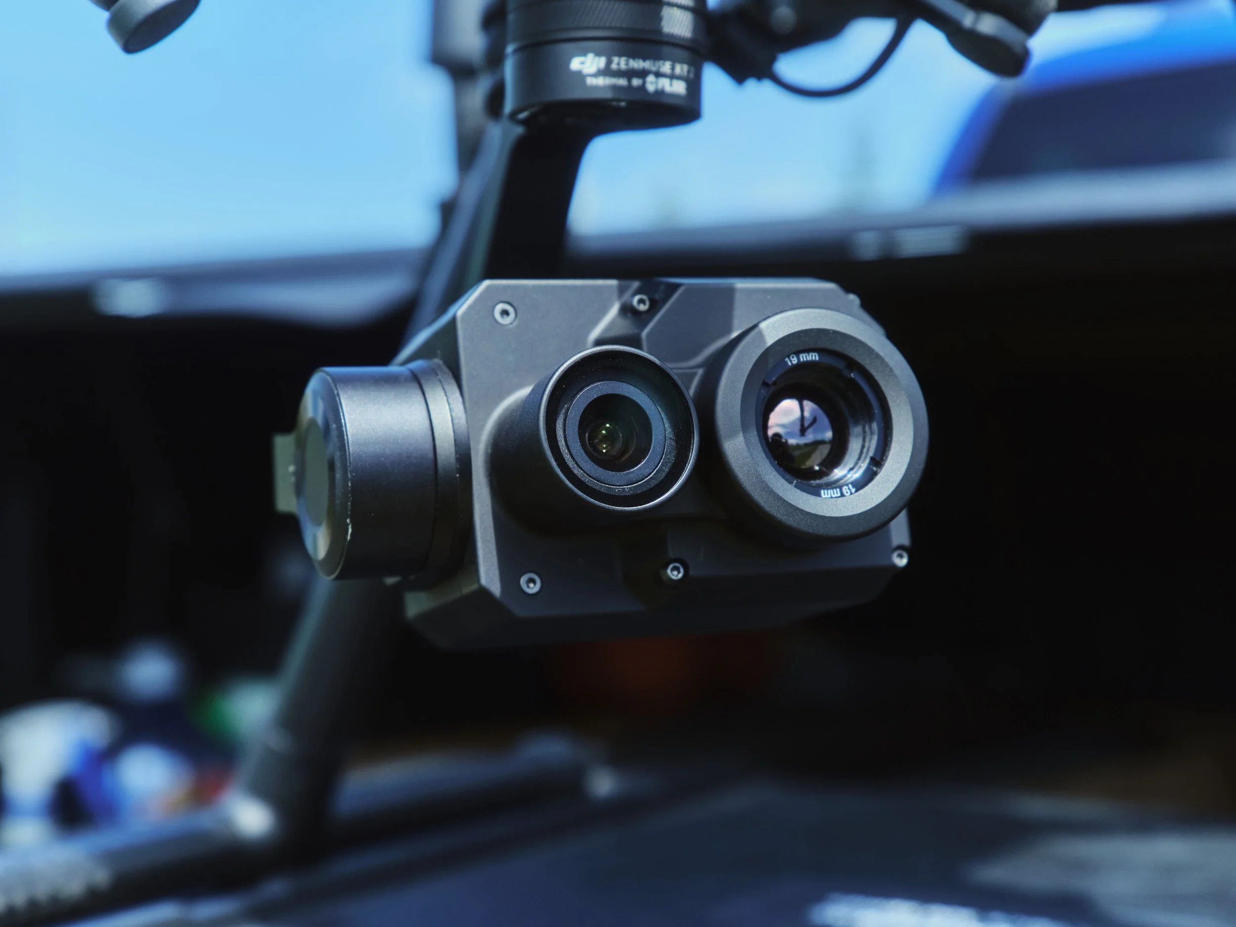 Close-up of a drone camera with two lenses and a black mount, with blue sky in the background.