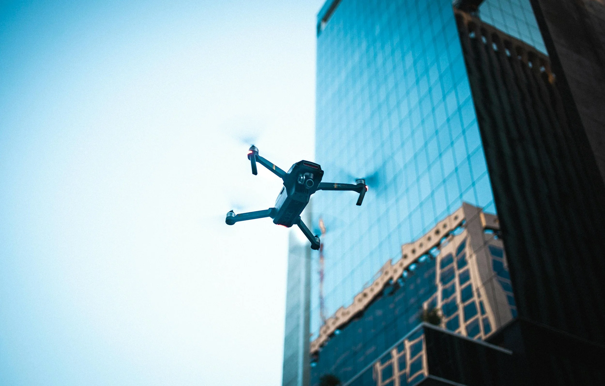 A drone flying in the sky next to a tall glass skyscraper.