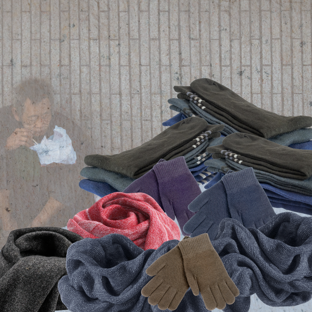 Shows  a homeless man sitting against the wall. In front of him is a table with socks, scarves, and gloves.