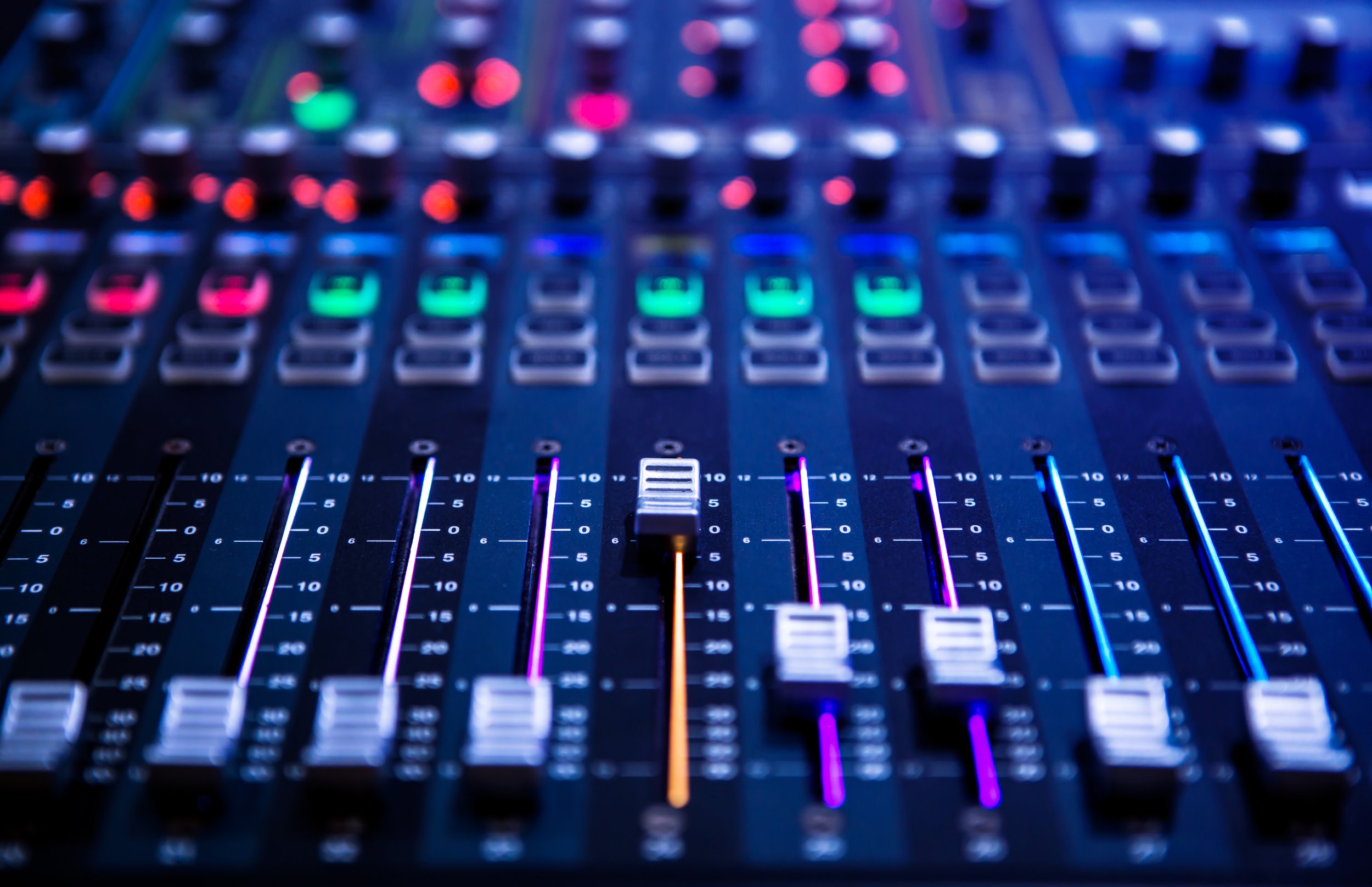 Close-up of a professional audio mixing console with colorful illuminated sliders and knobs.