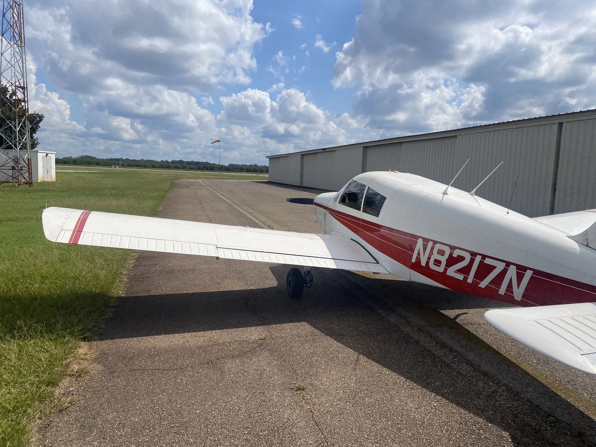 Small white airplane with red stripe and registration N8217N parked on a tarmac near a large hangar.