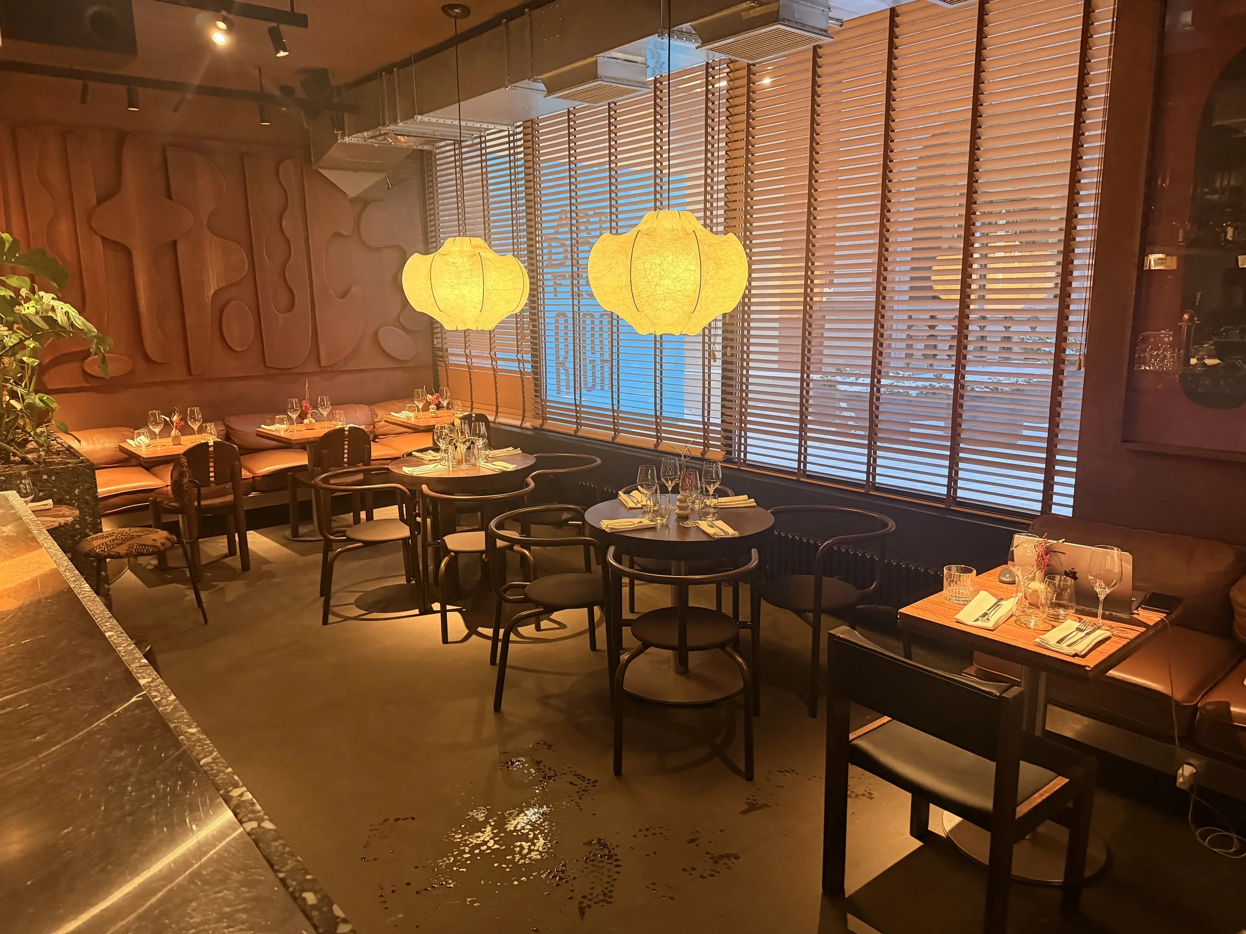 Cozy modern restaurant with warm lighting, round tables, and large windows, set up for an intimate dining or wine tasting experience.